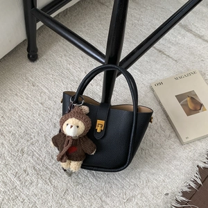 Detail of black pebbled leather bucket bag with gold clasp and cute bear charm accent