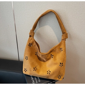 Detail of mustard yellow suede hobo bag with laser-cut floral patterns and tied strap