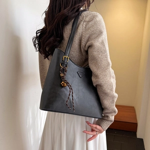 Detail of black leather tote bag with triangle patch and woven charm pendant