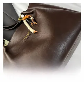 Détail d'un cabas en cuir marron foncé avec des perles en bois et un anneau en métal