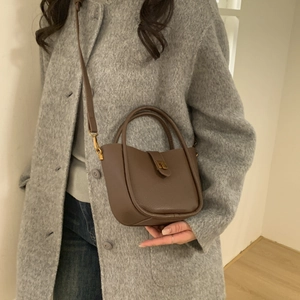Detailed view of a dark brown litchi leather bucket bag worn with a grey wool coat