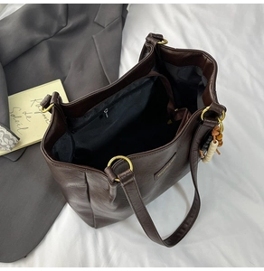 Détail d'un sac cabas en similicuir marron foncé avec pompon perlé et anneaux dorés