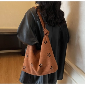 Close-up of laser-cut flower patterns and knot detail on a dark brown suede tote bag
