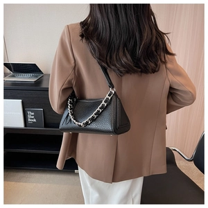 Detail of black pebbled leather handbag with silver chain and thin strap in office setting
