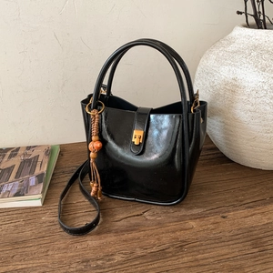 Détail d'un sac seau noir brillant avec un fermoir doré et un gland en perles de bois