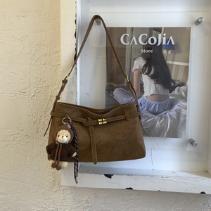 Detail of dark brown suede tote bag with metal buckle and teddy bear charm accessory