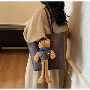 Close-up of a dark brown leather tote bag with a cute teddy bear charm and lychee texture