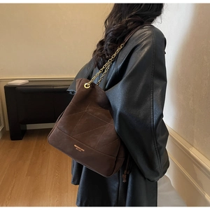 Detail of dark brown suede tote bag with quilted diamond pattern and gold chain strap