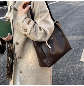 Détail du cabas en cuir marron foncé avec logo doré et breloque perlée sur manteau