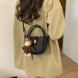Detail of black pebbled leather bucket bag with gold clasp and cute bear plush charm