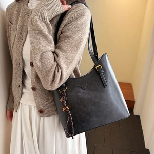 Detail of black matte tote bag featuring a triangle metal plaque and woven rope charm
