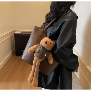 Detail of dark brown leather tote bag featuring a cute plush bear charm with NOIST text