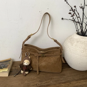 Detailed macro of brown suede tote bag featuring a metal lock and cute bear charm