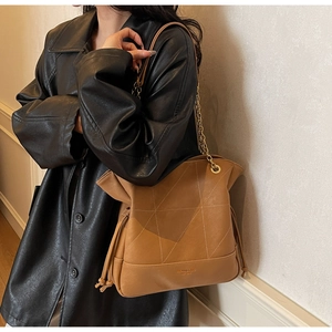 Detail view of brown quilted bucket bag with chain strap worn by a model in a black coat