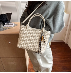 Detail of cream bucket bag with woven texture and wooden bead charm on a shoulder strap