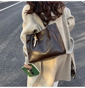 Détail du sac cabas en cuir marron foncé avec perles vintage sur un manteau en laine