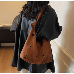 Detail of laser-cut flower patterns on dark brown suede shoulder bag with knotted strap