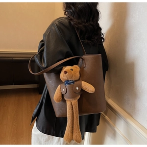 Detail of dark brown leather tote bag with a cute long-legged teddy bear plush pendant