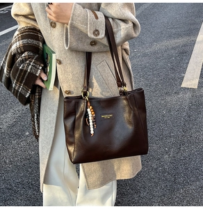 Détail d'un sac cabas en cuir mat marron foncé avec logo en métal et pompon en bois