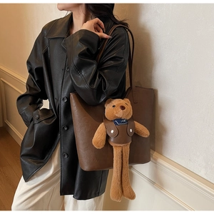 Detail of a large brown leather tote bag featuring a cute plush bear charm on a black coat