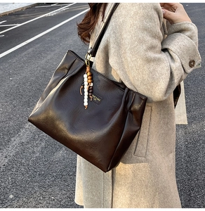 Détail du cabas plissé marron foncé avec breloque en bois sur un manteau en laine