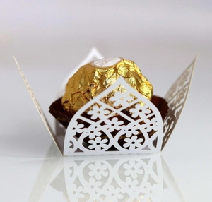 Macro shot of white laser-cut paper chocolate wrapper with intricate floral vine pattern