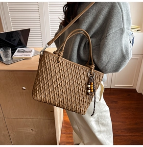 Detail of camel bucket bag with textured weave and wooden bead charm in office setting