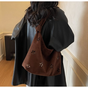 Detail of laser-cut floral pattern and knotted strap on brown faux suede shoulder bag