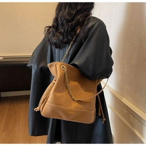 Detail of tan suede bucket bag with diamond stitching and gold chain strap on model