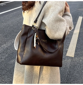 Détail d'un sac cabas en cuir marron foncé avec breloque décorative en perles et vue latérale