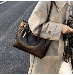 Détail d'un grand sac cabas marron foncé avec breloque en perles et texture cuir sur l'épaule