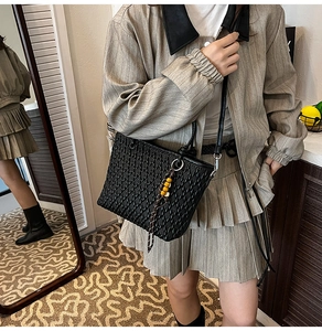 Detail of black woven leather tote bag with unique beaded tassel charm on a shoulder strap