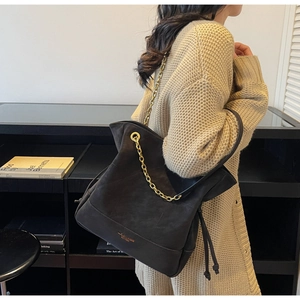 Detail of black matte bucket bag with golden chain strap and logo on model