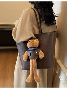 Deep brown faux leather tote bag with a plush teddy bear charm worn on shoulder