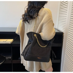 Close-up of black quilted suede tote bag featuring gold chain strap and brand lettering