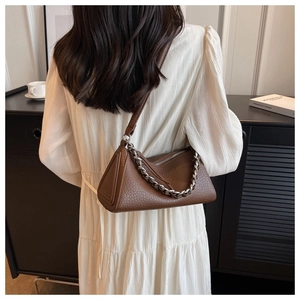 Detail of dark brown lychee leather underarm bag with silver chain and white pleated dress