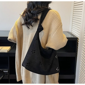 Close-up of black suede hobo bag featuring floral laser-cut patterns and knotted strap