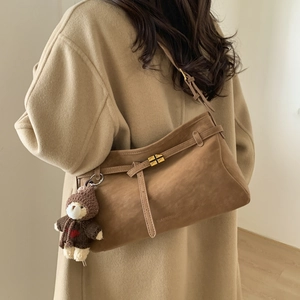 Detail of brown suede tote bag with gold cross-lock and cute teddy bear charm