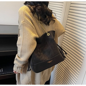Detail of black quilted bucket bag with gold chain strap and drawstring on model
