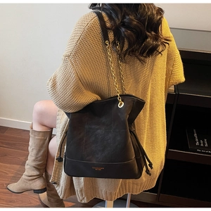 Detail of black quilted bucket bag with gold chain strap and drawstring sides