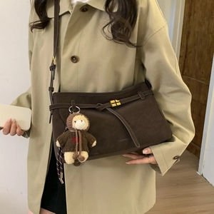 Detail of dark brown suede tote bag with golden cross clasp and cute teddy bear charm