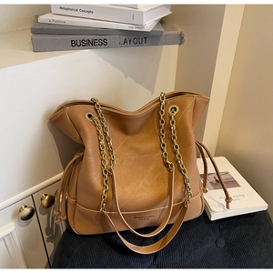 Detail of caramel bucket bag showing quilted texture, drawstring, and gold chain strap