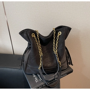 Detail of black leather bucket bag with gold chain strap and drawstring closure