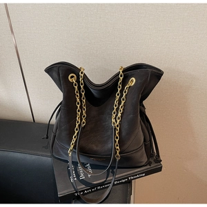Detail shot of black quilted leather bucket bag featuring a thick gold chain strap and drawstring