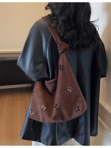 Brown suede underarm bag with knot detail and laser-cut floral patterns on model