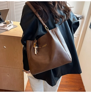Détail du sac cabas marron foncé avec écusson logo vintage et pendentif à pompon perlé