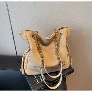 Detail of large beige bucket bag with gold chain strap and drawstring side on design book