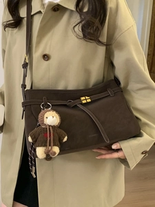 Stylish dark brown tote bag with gold buckle and cute bear pendant on a trench coat model