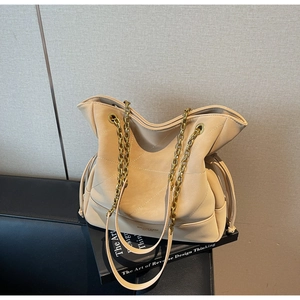 Close-up of quilted beige bucket bag with gold chain strap and drawstring details