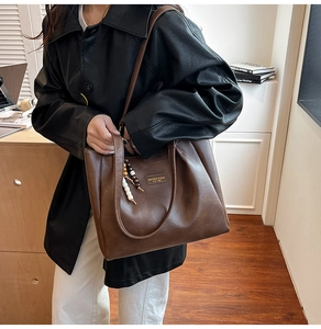 Détail du sac cabas vintage en cuir marron avec breloque en bois et logo métallique